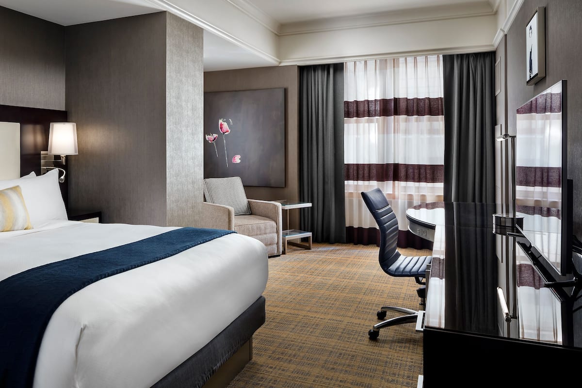 A hotel room with a large bed, a desk, a chair, and a painting on the wall.