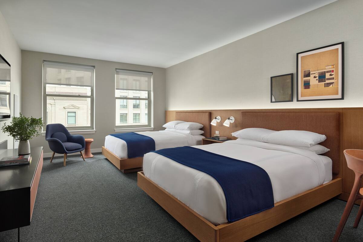 A hotel room with two beds, a desk, a chair, and a large window.