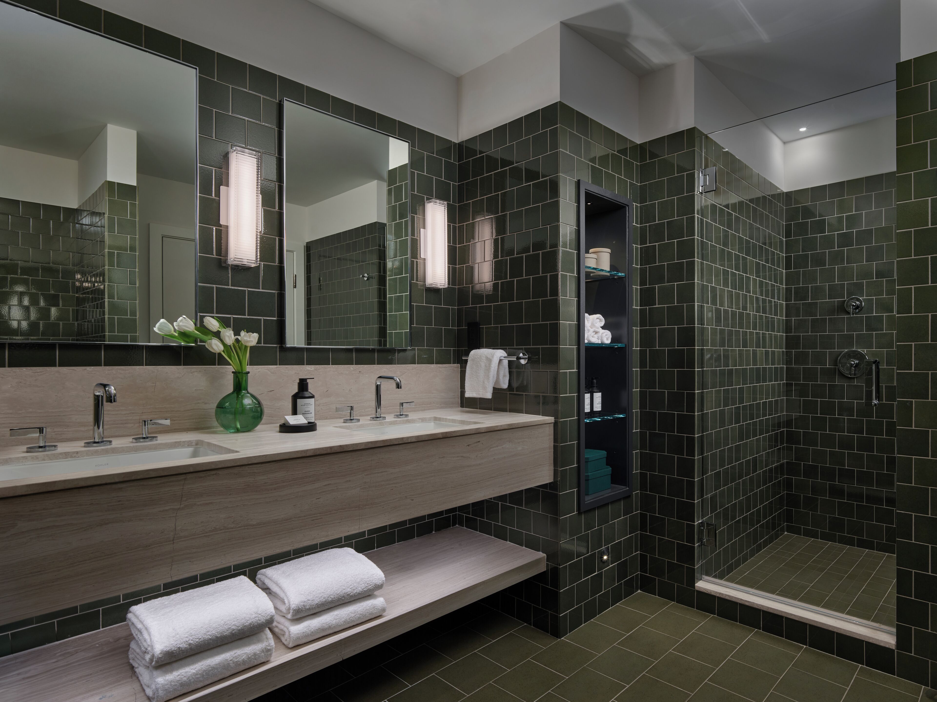 Un baño moderno con tocador doble lavamanos, un espejo grande y zona de ducha con azulejos oscuros.
