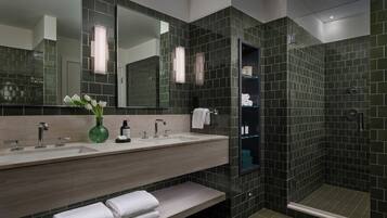 Un baño moderno con tocador doble lavamanos, un espejo grande y zona de ducha con azulejos oscuros.
