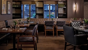 Un ristorante con un'area salotto accogliente, tavoli in legno e vista sulla strada attraverso ampie finestre.