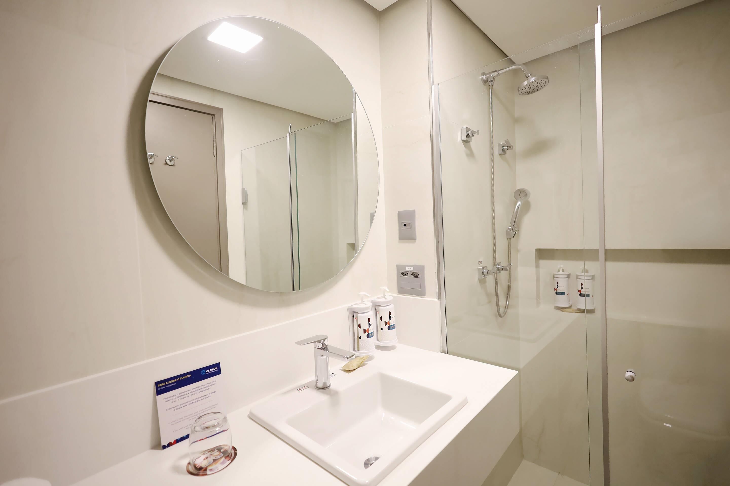 A modern bathroom with a round mirror, a white sink, and a glass-enclosed shower.