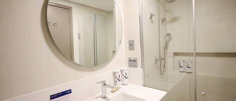 A modern bathroom with a round mirror, a white sink, and a glass-enclosed shower.