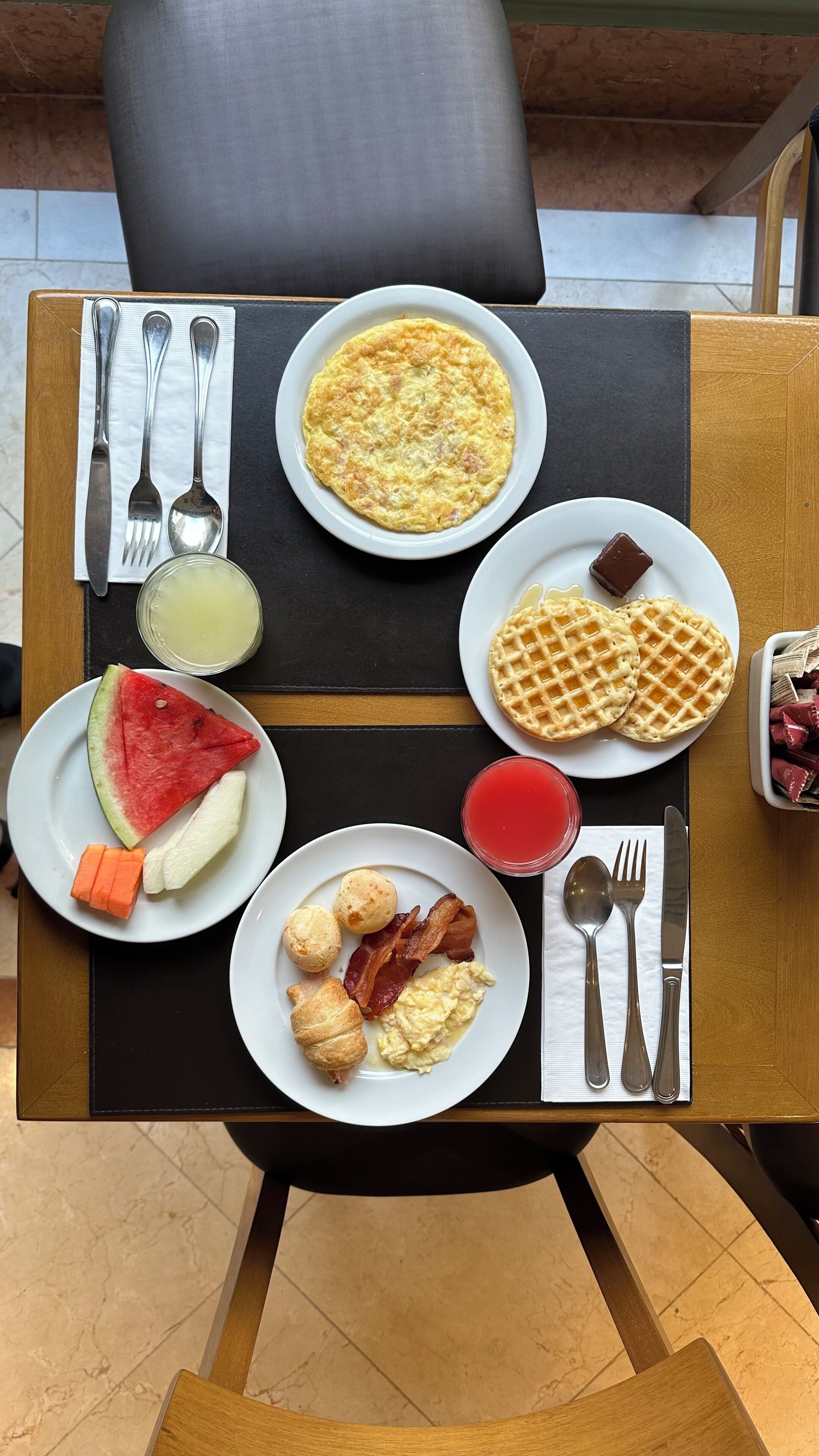 A breakfast table with plates of eggs, waffles, toast, and a bowl of fruit.