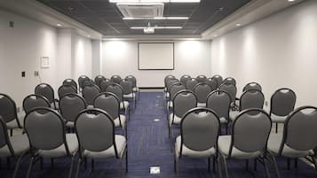 A conference room with rows of chairs, a projector screen, and a carpeted floor.
