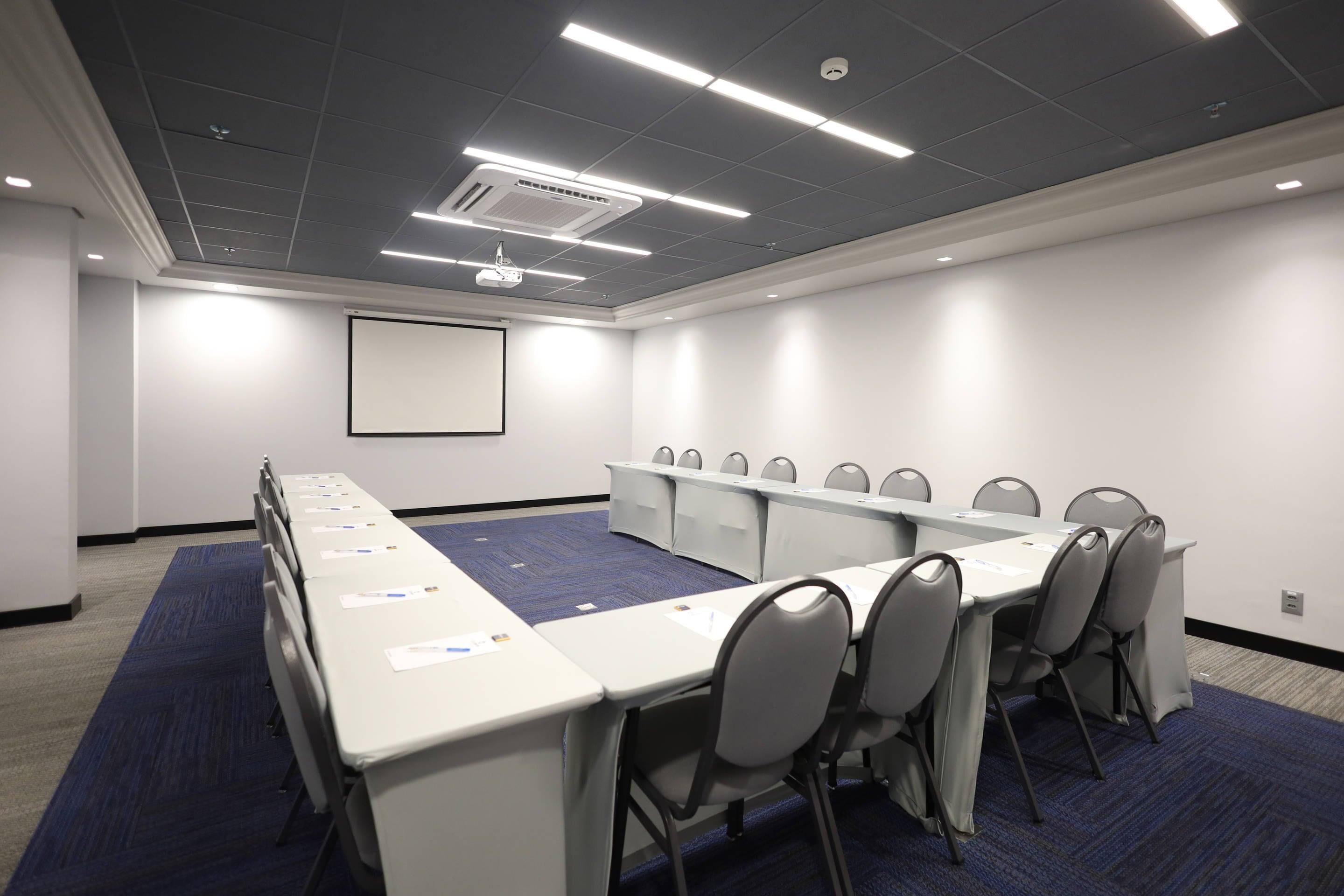 Un salón de conferencias con una larga mesa, sillas, una pantalla de proyector y una pizarra.