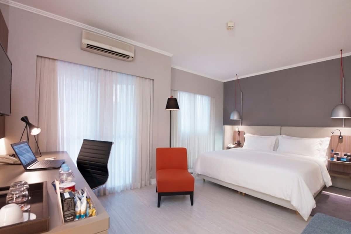 A hotel room with a bed, desk, chair, and a standing lamp.