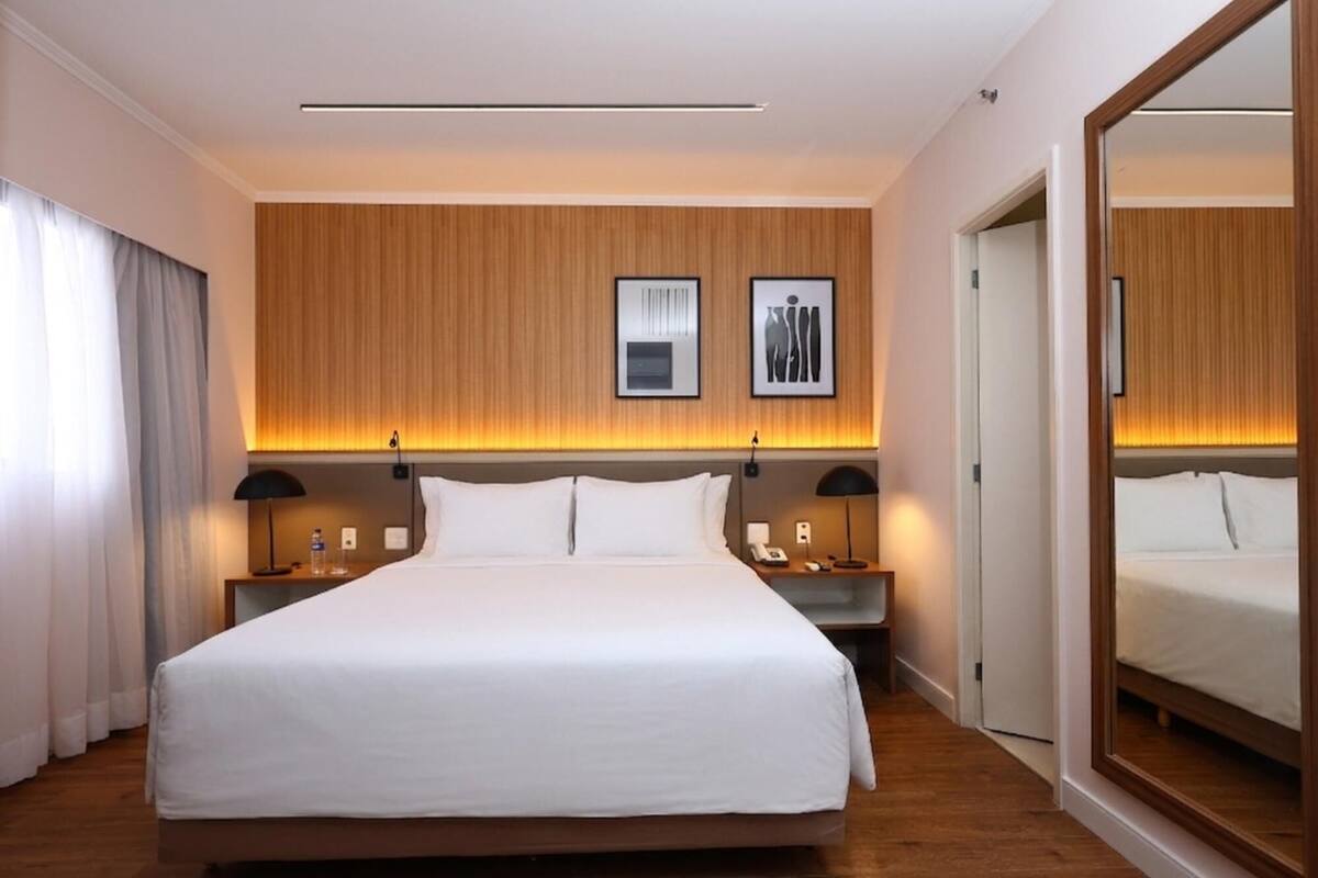 A hotel room with a large bed, wooden panel wall, two bedside tables with lamps, and a large mirror.