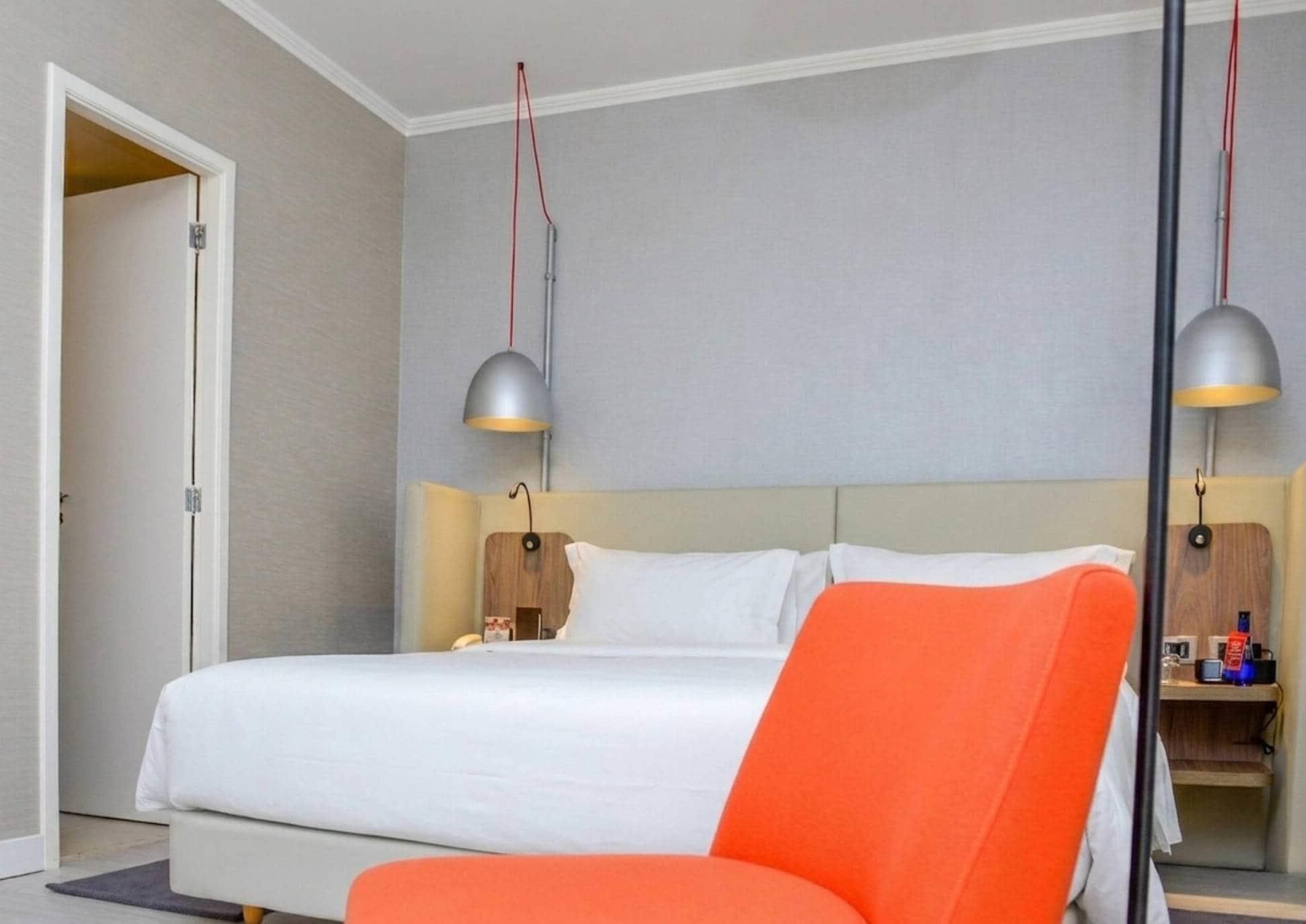 Una habitación de hotel con una cama, una mesita de noche, una lámpara y una silla.