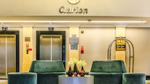 A hotel lobby with a chandelier, two elevators, green sofas, a round coffee table, and a sign that reads "Clarion." - Clarion Hotel Faria Lima (São Paulo)