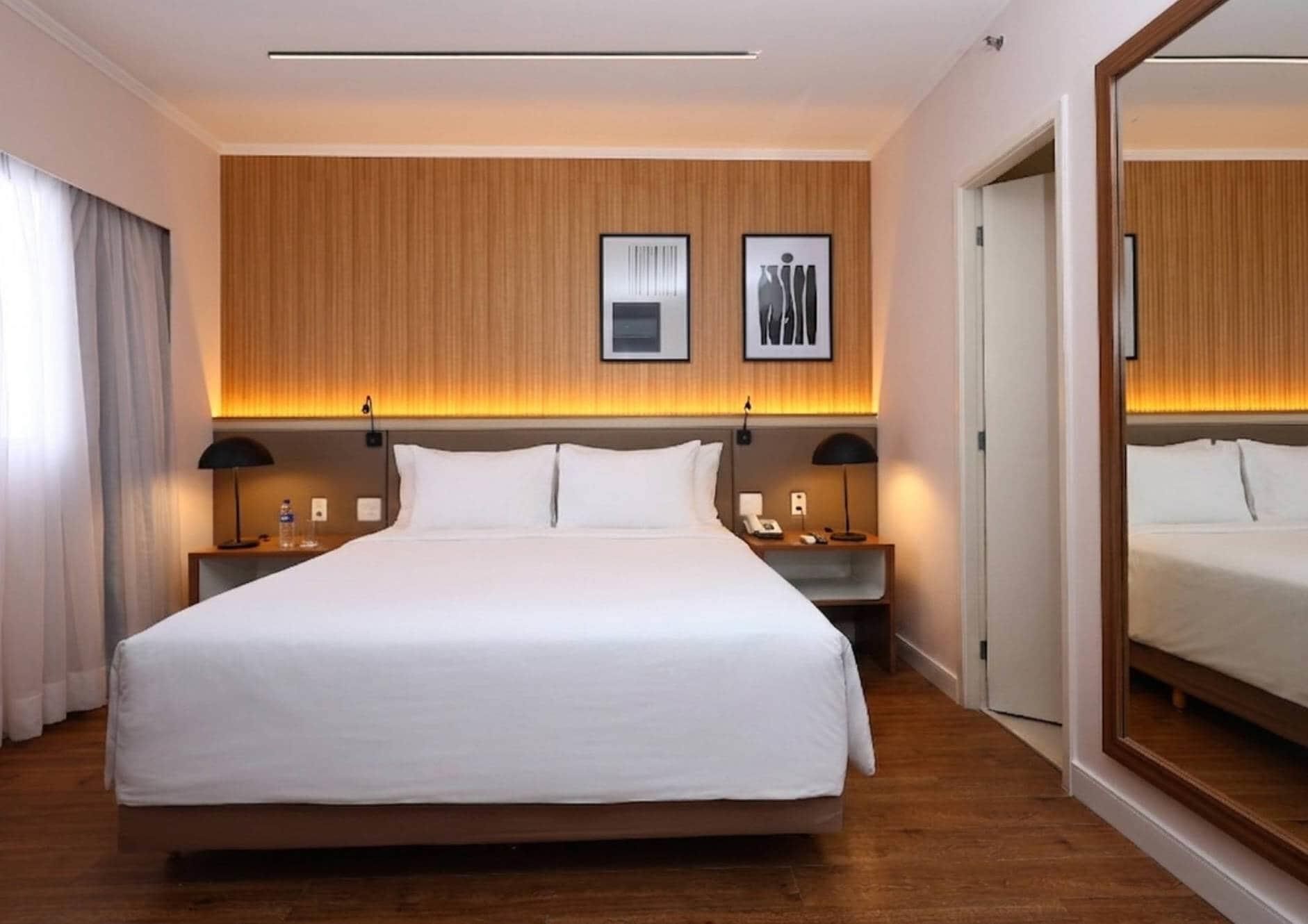 A hotel room with a large bed, two bedside tables, a mirror, and wooden paneling on the walls.
