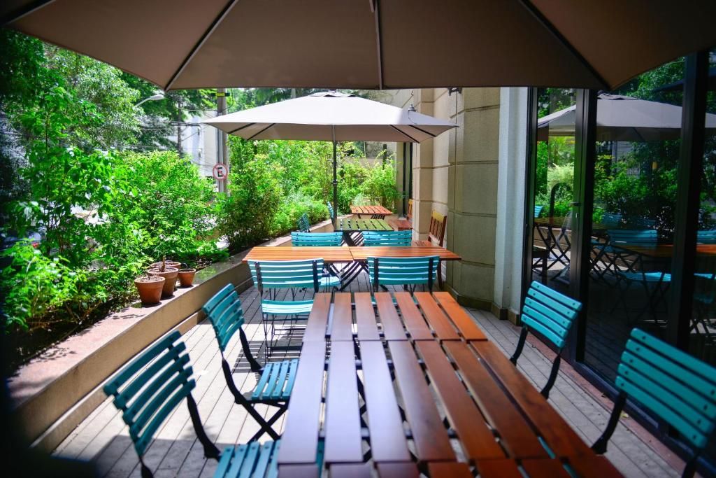 Een terras buiten met houten tafels en banken, omgeven door groen.