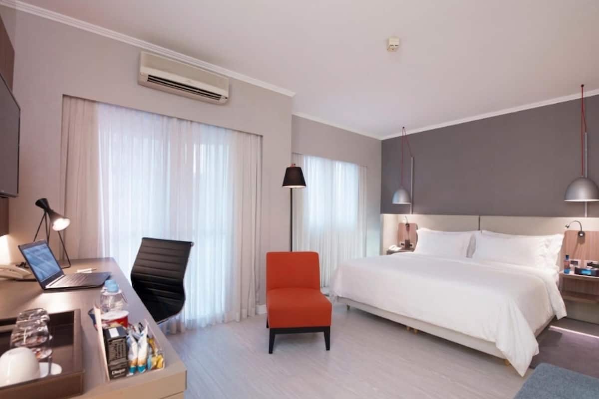 A hotel room with a bed, desk, chair, and a standing lamp.
