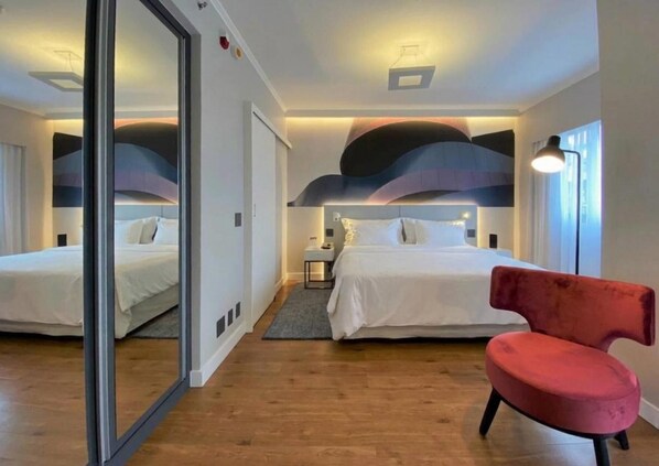 A hotel room with two beds, a red chair, and a modern ceiling design. - Clarion Hotel Faria Lima (São Paulo)