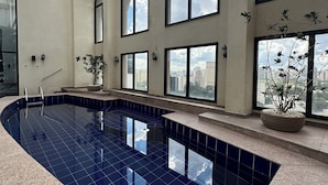 An indoor swimming pool with a glass ceiling, multiple windows, and a view of the cityscape. - Clarion Hotel Faria Lima (São Paulo)