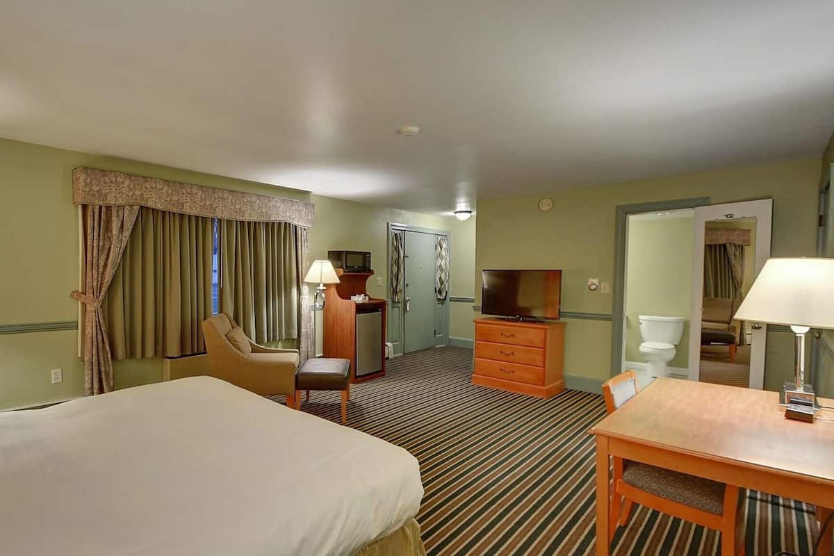 Quarto de hotel com duas camas, uma escrivaninha, uma cadeira, televisão, cômoda e porta para o banheiro.