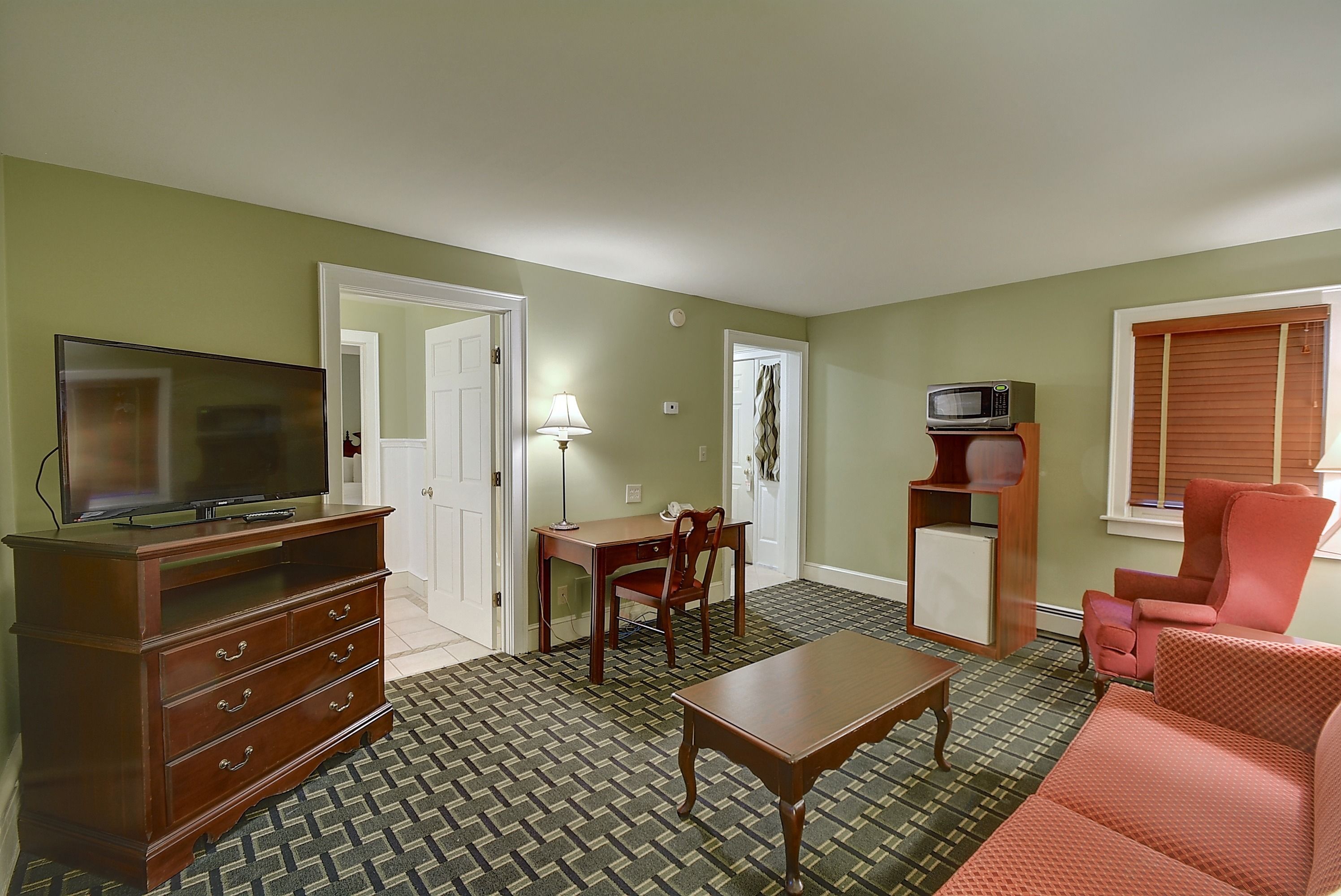 A living room with a television, a wooden dresser, a dining table, and a red sofa.