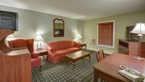 A hotel room with a sofa, a coffee table, a desk with a telephone, a mirror, and a television. - Colonial Motel (Brattleboro)