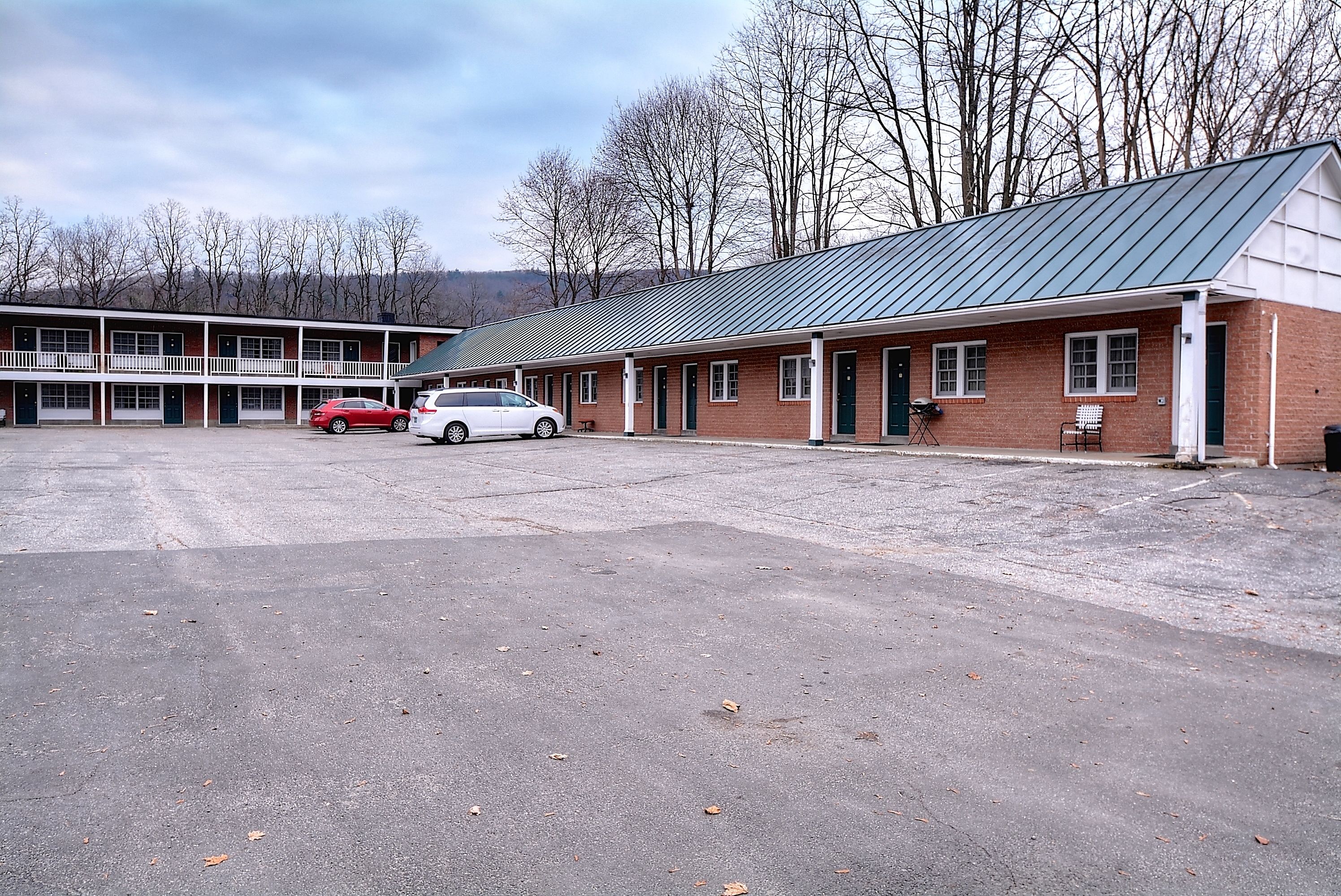 A motel with a parking lot, a brick building, and a row of rooms with a green roof.
