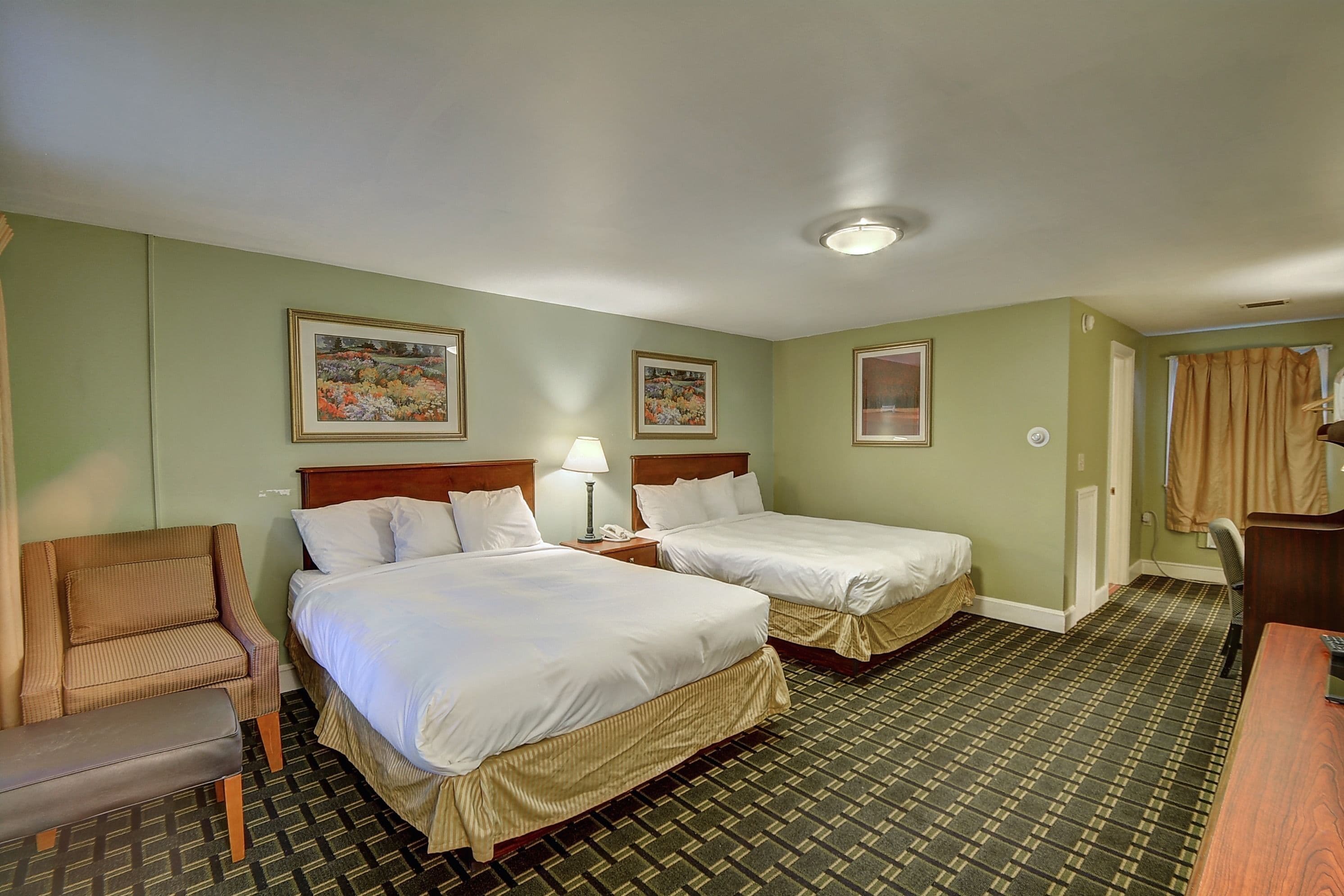 A hotel room with two beds, a chair, a desk, and a lamp.