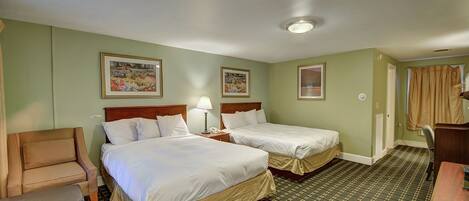 A hotel room with two beds, a chair, a desk, and a lamp.