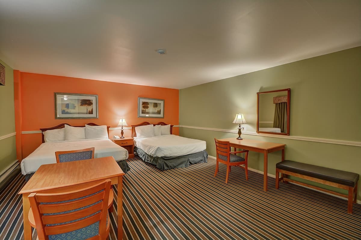 Quarto de hotel com duas camas, uma escrivaninha, uma cadeira, um banco e um espelho.