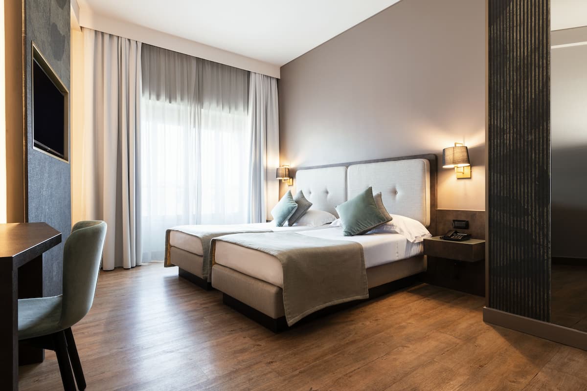 A hotel room with a bed, bedside tables, a desk, and a chair.