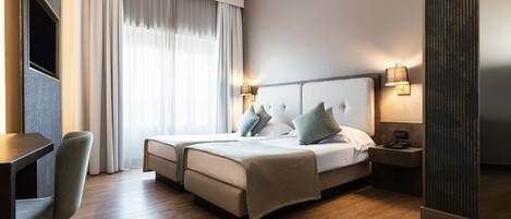 A hotel room with a bed, bedside tables, a desk, and a chair.