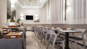 A modern dining area with a long table, chairs, and a buffet with fruits and drinks.