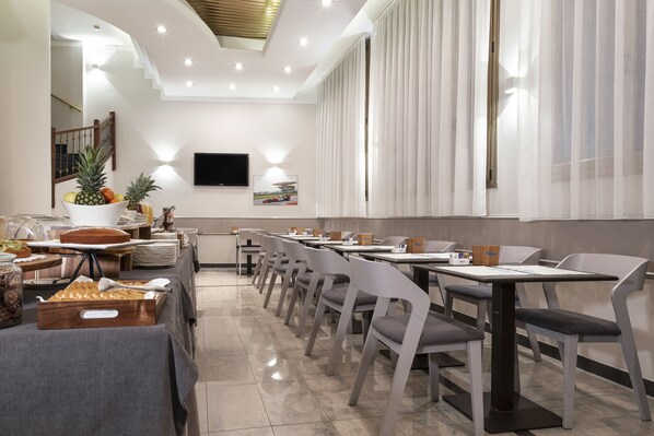 A modern dining area with a long table, chairs, and a buffet with fruits and drinks.