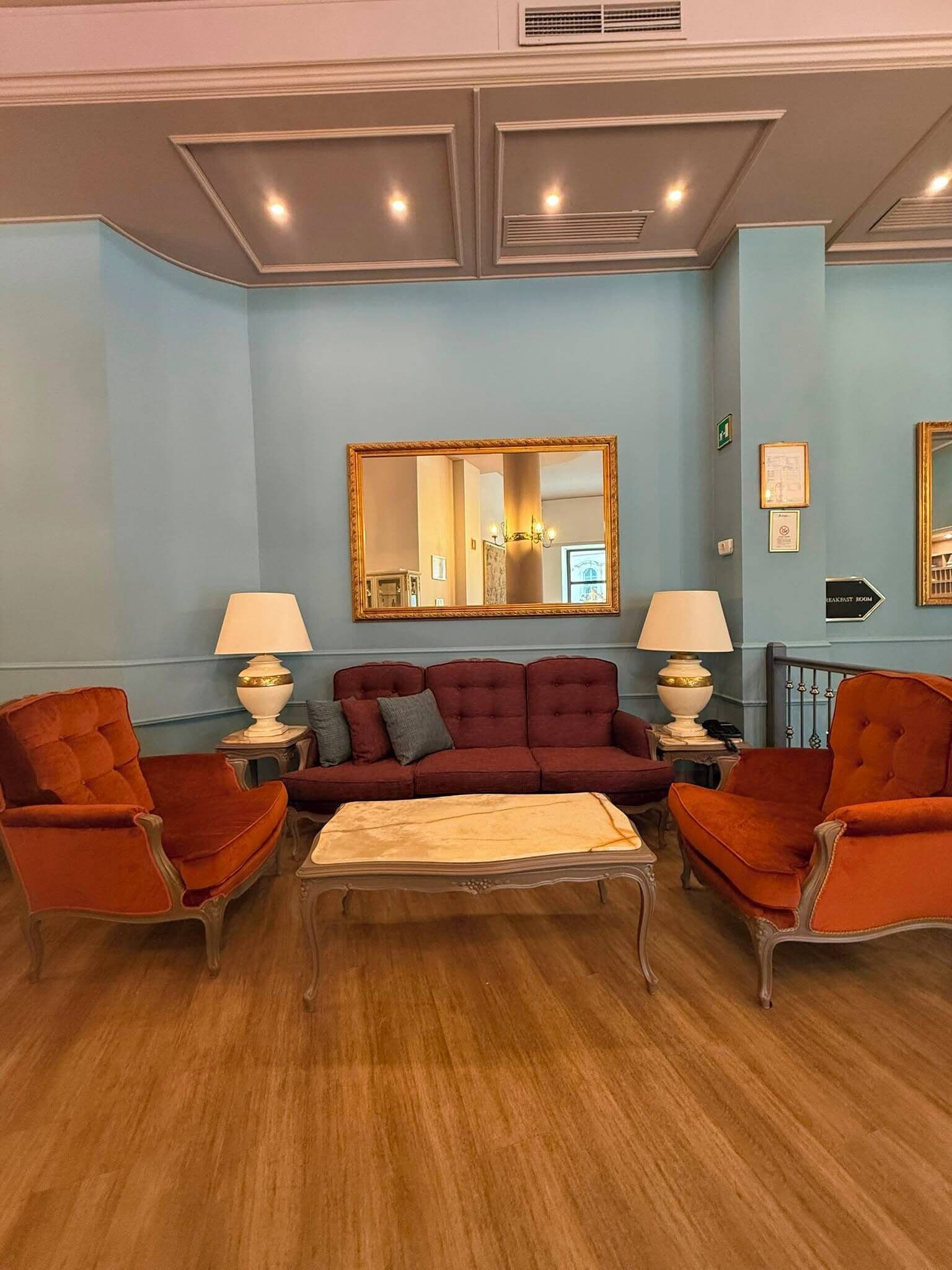 Una habitación con sofá, dos sillones, una mesita de centro, un espejo y un letrero que indica el comedor.