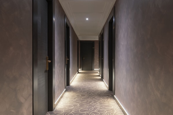 A long, narrow hallway with dark walls and a patterned carpet. - Mokinba Hotels King (Milan)