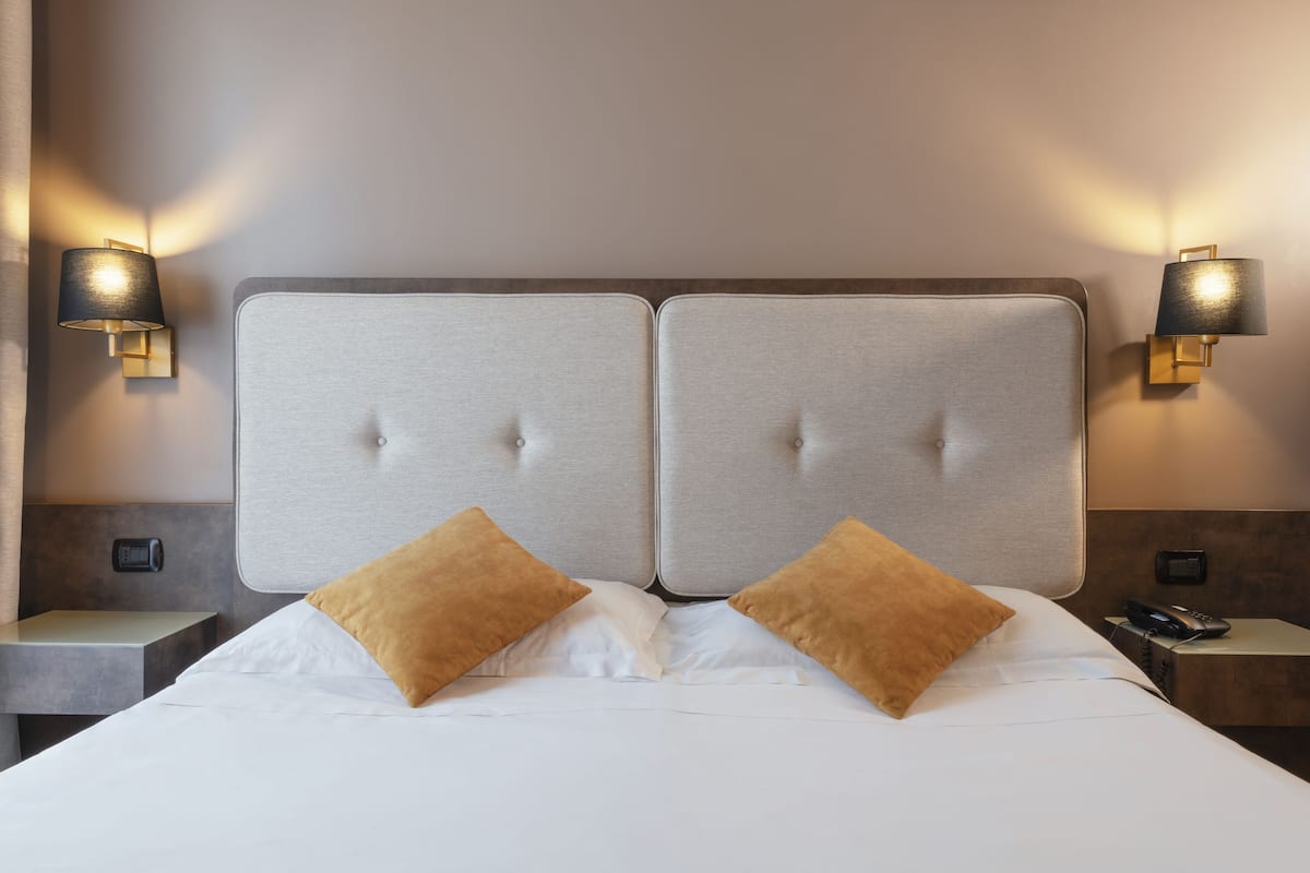 A double bed with two pillows, a headboard with a tufted design, and two wall-mounted lamps.