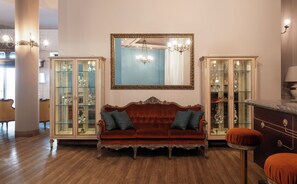 Una habitación con un sofá de terciopelo rojo, dos vitrinas de vidrio y un espejo grande con marco dorado.