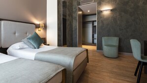 A modern hotel room with two beds, a seating area, and a wardrobe.