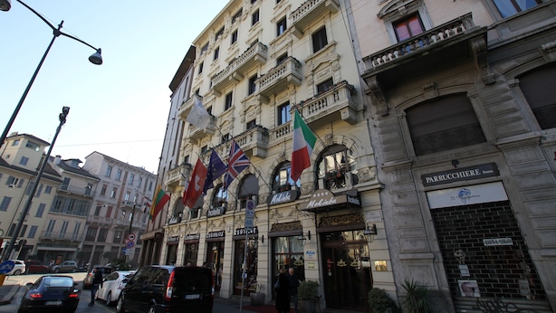 A hotel facade with multiple balconies, a sign for 'PARRUCHIERE', and flags.