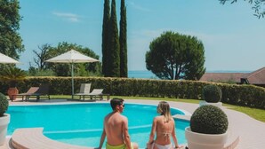Ein Paar sitzt am Pool mit Meerblick, umgeben von Topfpflanzen und Liegestühlen.