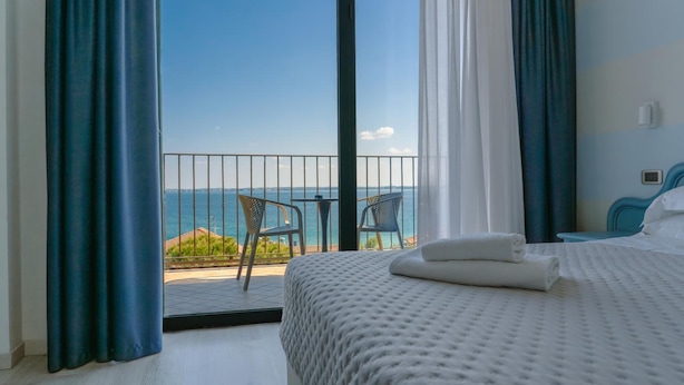 Ein Hotelzimmer mit Bett, einem Balkon mit Tisch und Stühlen sowie Blick auf das Meer.