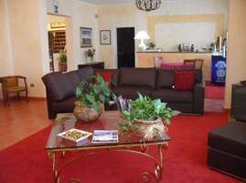 Una sala de estar con un sofá marrón, una mesa de centro de vidrio y dos plantas en macetas.