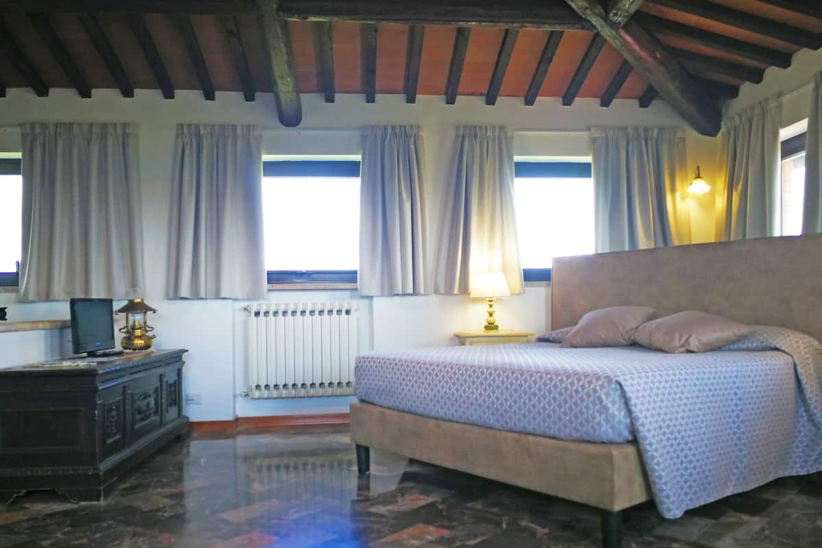A bedroom with a bed, a nightstand with a lamp, a dresser, and a window with curtains.