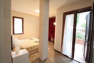 A bedroom with a bed, a nightstand, a window, and a door leading to a balcony.
