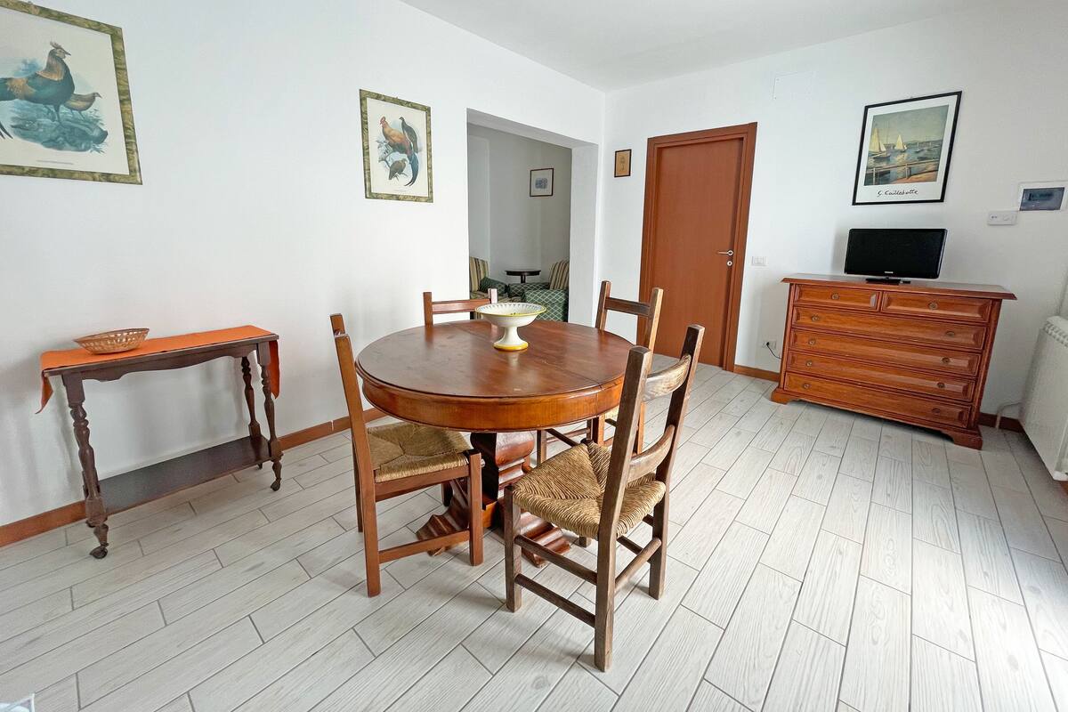 A dining area with a wooden table and chairs, a small side table, and a dresser with a television.