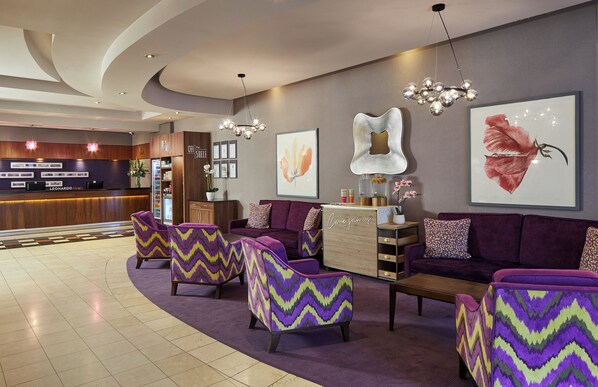 Un hall d’entrée avec un comptoir de réception, des canapés violets et des fauteuils à motifs chevrons.