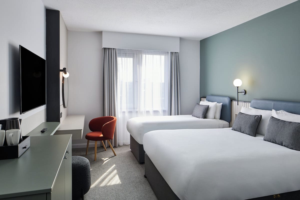 Una habitación de hotel con una cama, un escritorio con televisor, una silla y una ventana con cortinas.