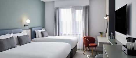 A hotel room with two beds, a desk with a TV, a chair, and a window with curtains.