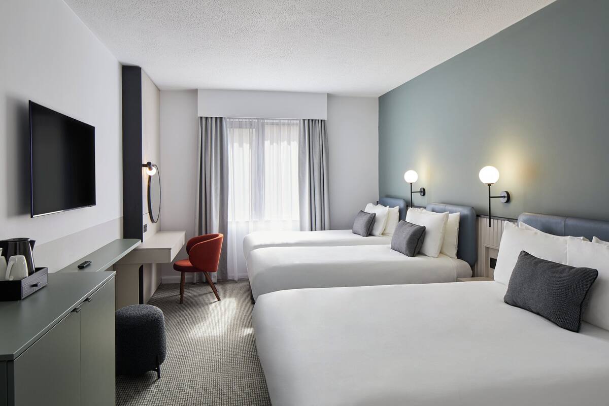 A hotel room with two beds, a desk, a TV, and a chair.