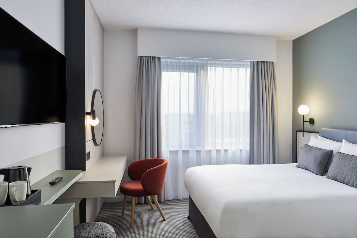 Habitación de hotel con cama, escritorio, silla, televisión y ventana con cortinas.
