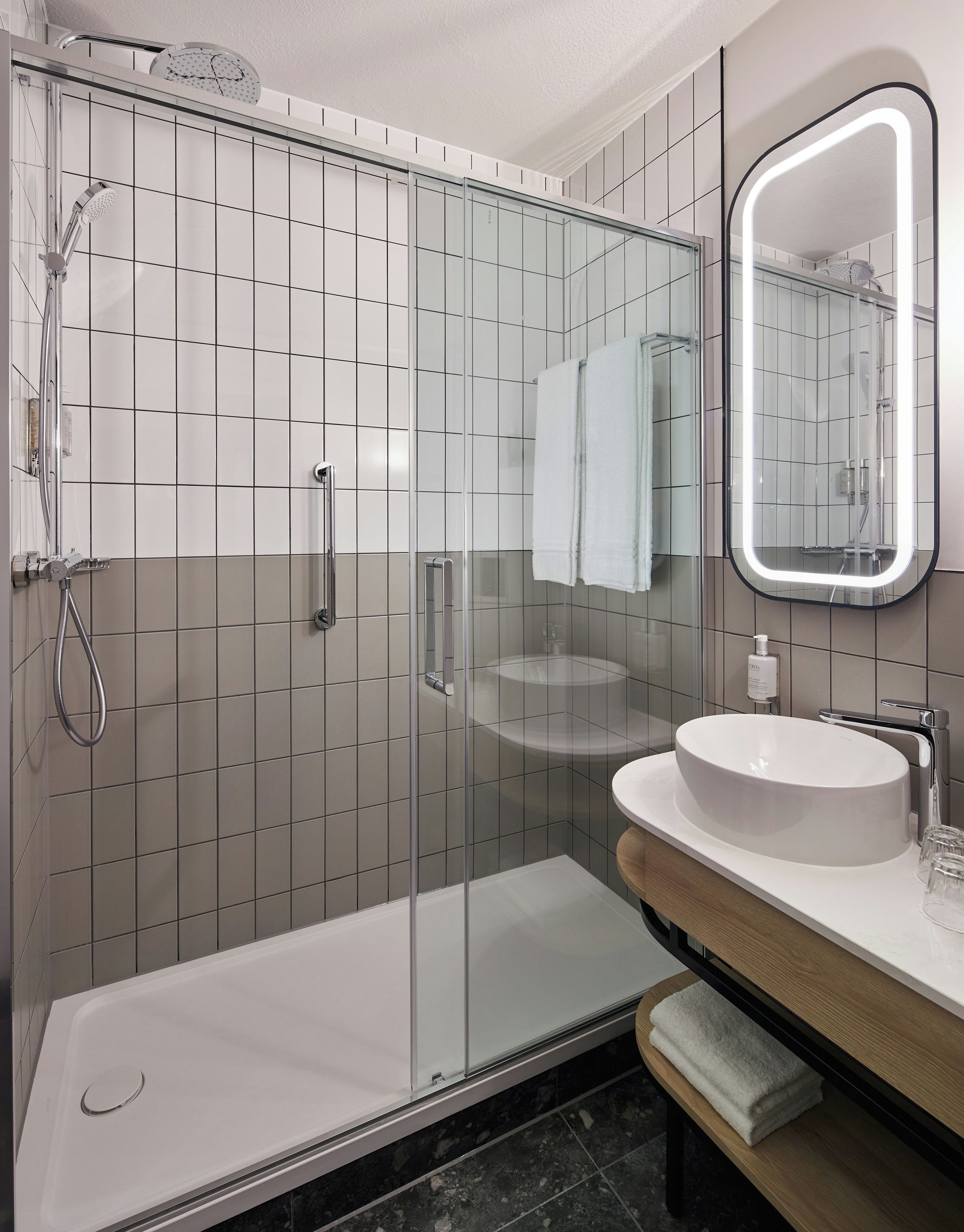 Un baño moderno con ducha de vidrio, lavamanos blanco y espejo con marco iluminado.