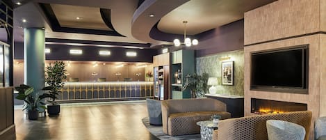 A hotel lobby with a reception desk, seating area, and a large flat-screen TV mounted on the wall.