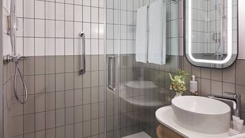 Un baño moderno con ducha de mampara de vidrio, lavamanos blanco y un espejo grande.